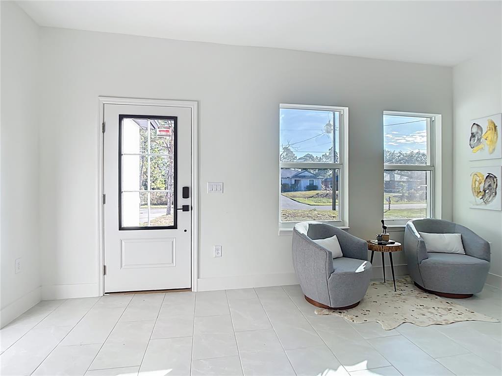 A bright entryway features white walls, light tile flooring, two gray armchairs, and a front door — 422 EISENHOWER BOULEVARD, LEHIGH ACRES, FL