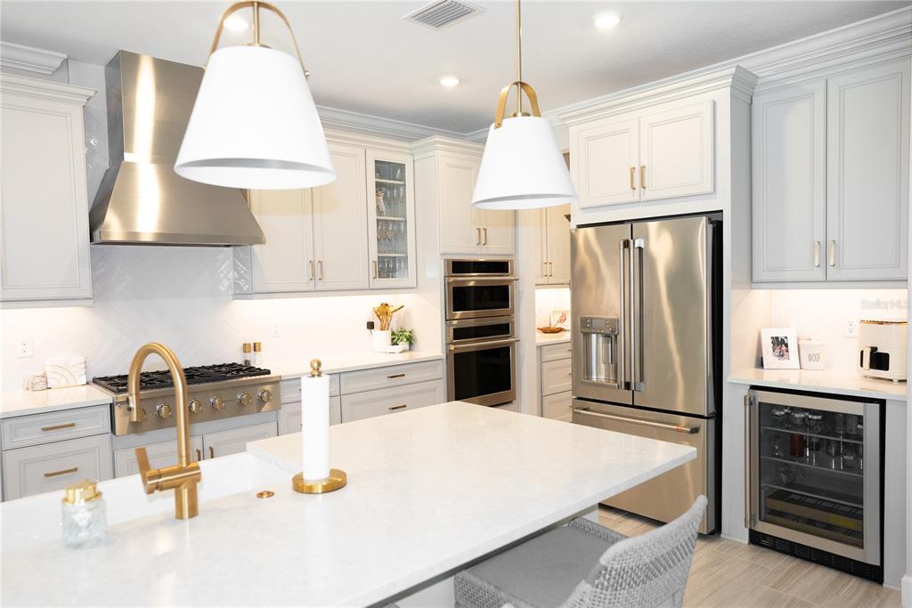 A modern kitchen features white cabinetry, stainless steel appliances, gold hardware, and a large island — 9217 TORRENT TRAIL, SARASOTA, FL