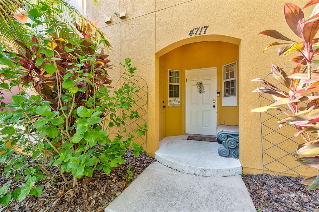 A concrete walkway leads to the white front door of a yellow stucco building entrance — 4717 FLAGLER BEACH WAY, KISSIMMEE, FL