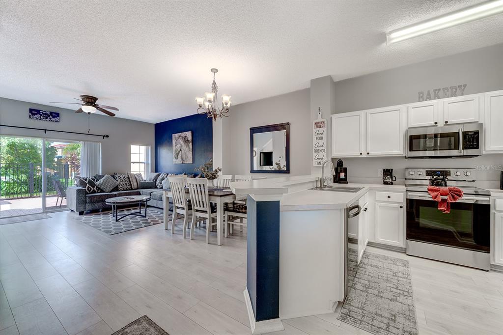 An open-concept kitchen and living area featuring white cabinets, a dark blue accent wall, and wood-look flooring — 4717 FLAGLER BEACH WAY, KISSIMMEE, FL