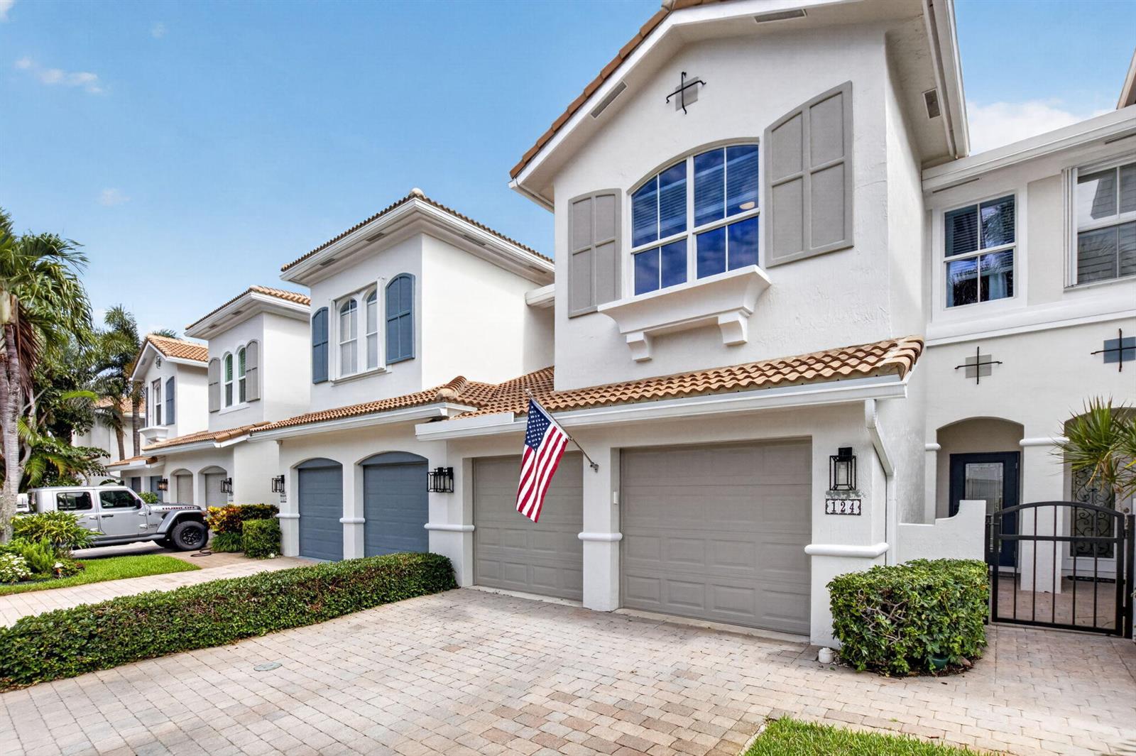 A row of white townhouses with gray garage doors and a displayed American flag — 124 Las Brisas Circle, Hypoluxo FL 33462, HYPOLUXO, FL