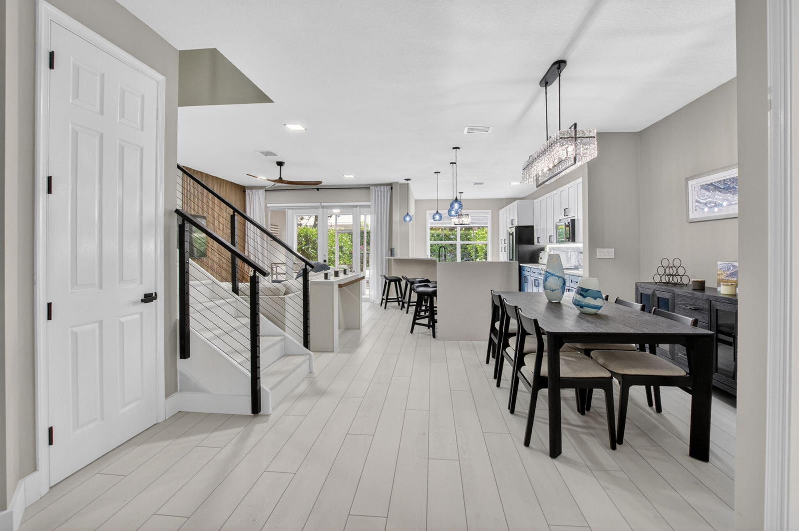 An open-concept living area features a dining table, kitchen island, and a staircase with railings — 124 Las Brisas Circle, Hypoluxo FL 33462, HYPOLUXO, FL