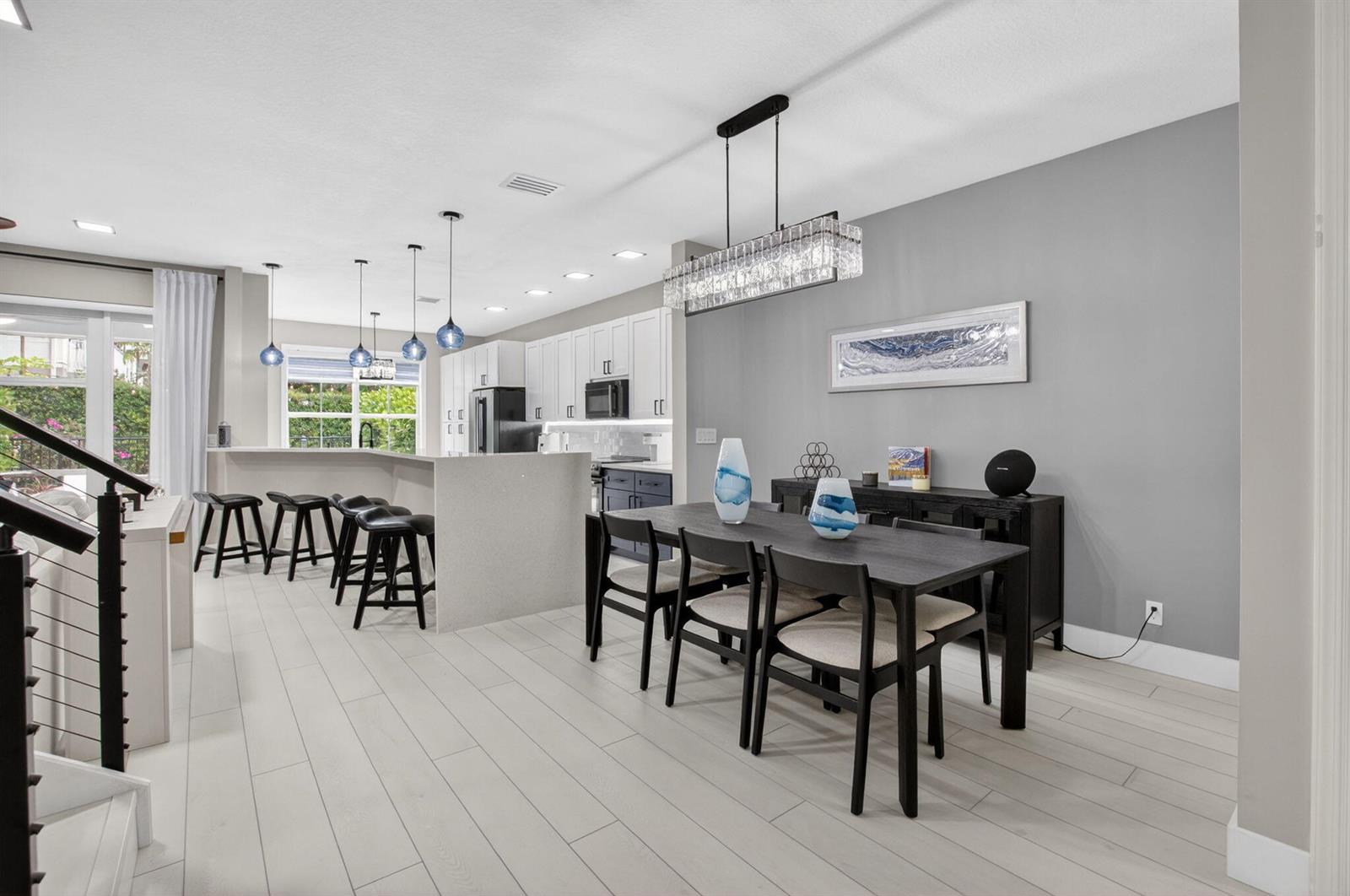 A dining area with a dark table and chairs sits next to a modern kitchen — 124 Las Brisas Circle, Hypoluxo FL 33462, HYPOLUXO, FL