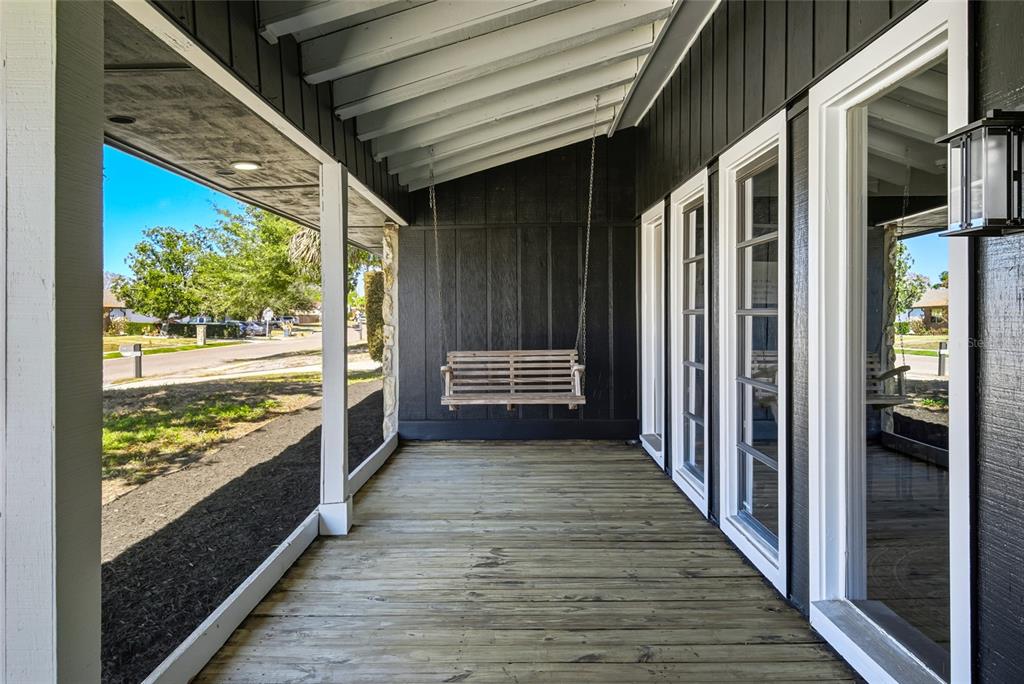 A covered wooden porch features a hanging bench swing against a dark vertical-plank wall — 213 DOVERWOOD ROAD, FERN PARK, FL