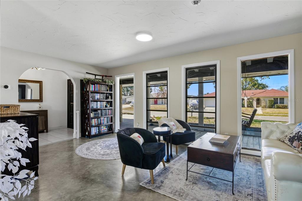 A living room features concrete floors, a bookshelf, two dark armchairs, and large windows — 213 DOVERWOOD ROAD, FERN PARK, FL
