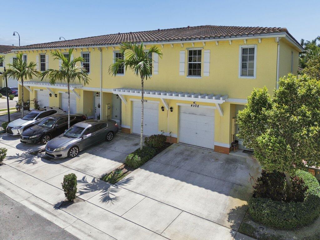An exterior view of a yellow two-story townhouse complex with attached garages and palm trees — 4008 NW 11th Drive, Lauderhill FL 33313, LAUDERHILL, FL