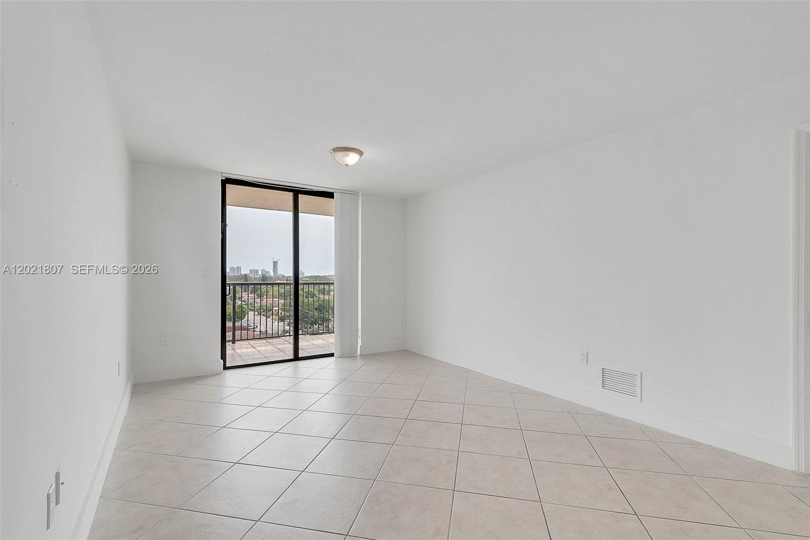 An empty room features white walls, light-colored tile flooring, and a sliding glass balcony door — 1690 SW 27th Ave # 805, Miami FL 33145, MIAMI, FL