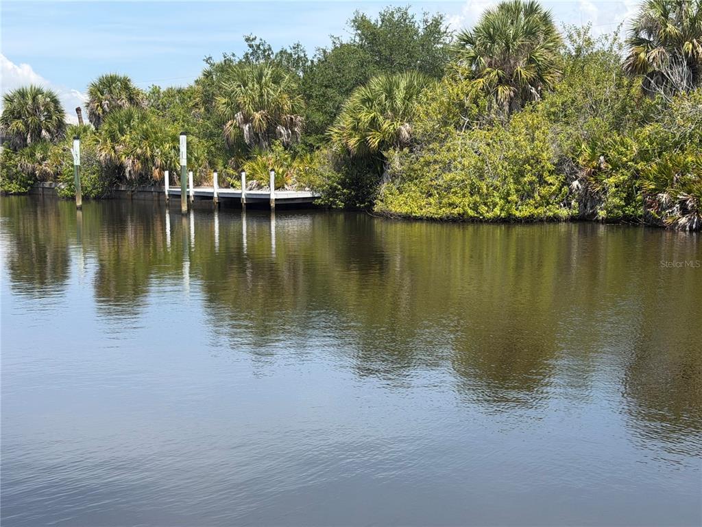 A wooden dock sits along a canal bank surrounded by lush tropical trees and palms — 17163 EDGEWATER DRIVE, PORT CHARLOTTE, FL