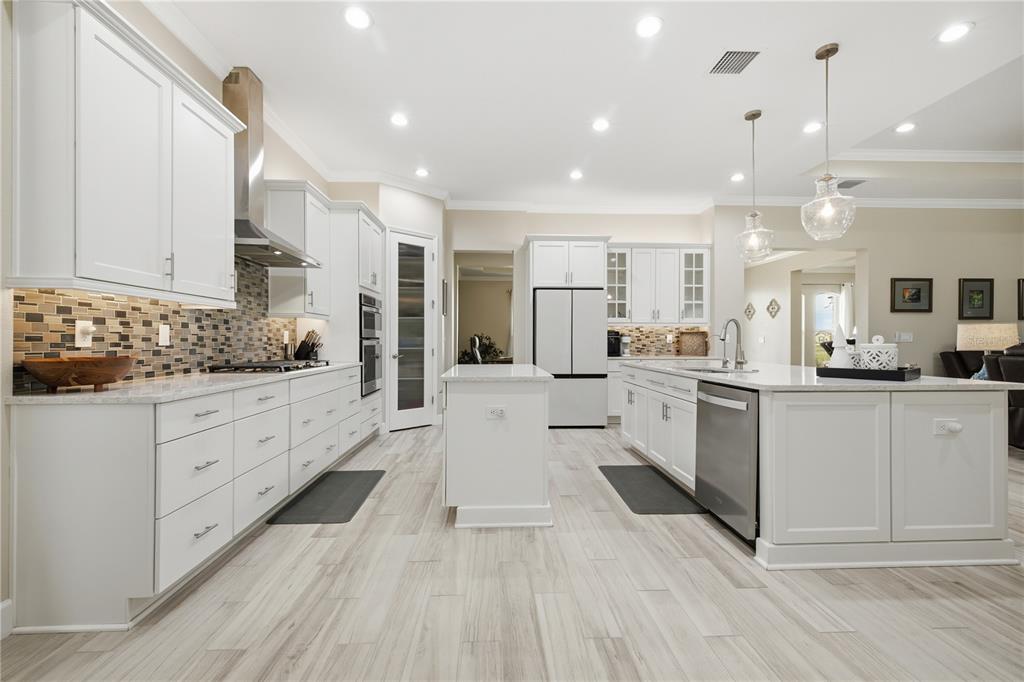 A modern kitchen features white cabinetry, stainless steel appliances, a center island, and wood-look flooring — 5315 SAN REMO CIRCLE, WIMAUMA, FL