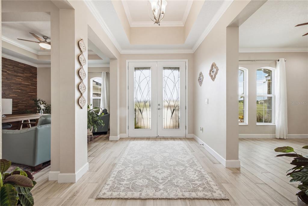 A bright entryway features a tray ceiling, double glass-paneled doors, and light-colored wood-look tile flooring — 5315 SAN REMO CIRCLE, WIMAUMA, FL