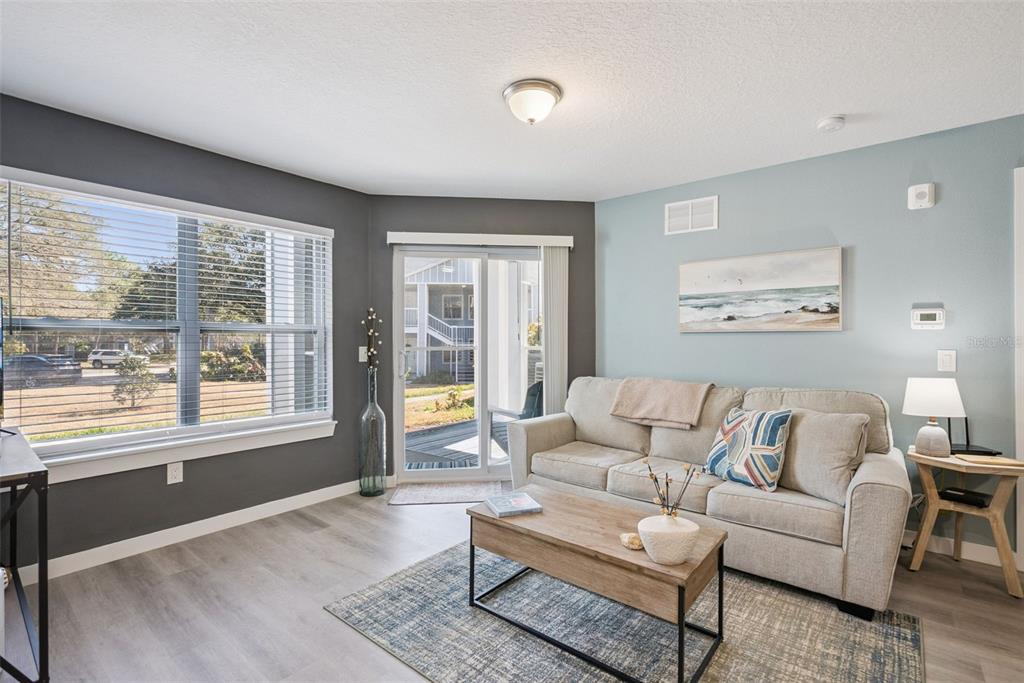 A living room features gray and light blue walls, wood-look flooring, and a sliding glass door — 2592 GRASSY POINT DRIVE UNIT 112, LAKE MARY, FL
