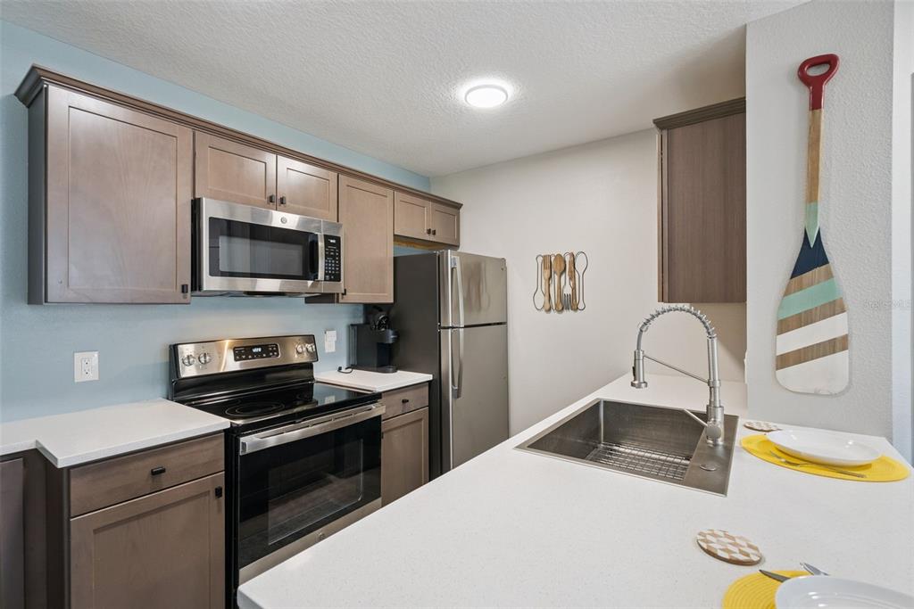 A kitchen with stainless steel appliances, wood cabinets, white countertops, and a sink island — 2592 GRASSY POINT DRIVE UNIT 112, LAKE MARY, FL