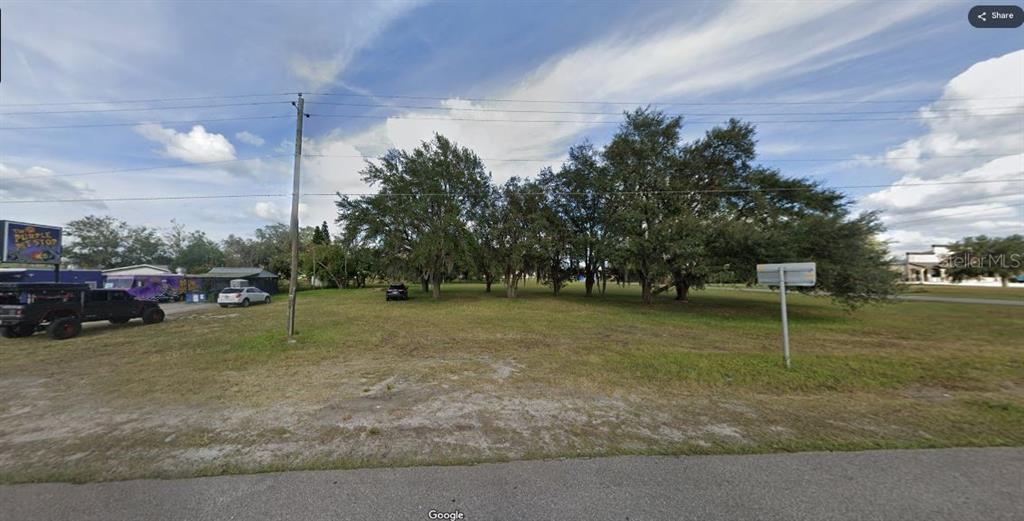 A vacant, grassy lot with several mature trees sits next to a small commercial building — N/A, POLK CITY, FL