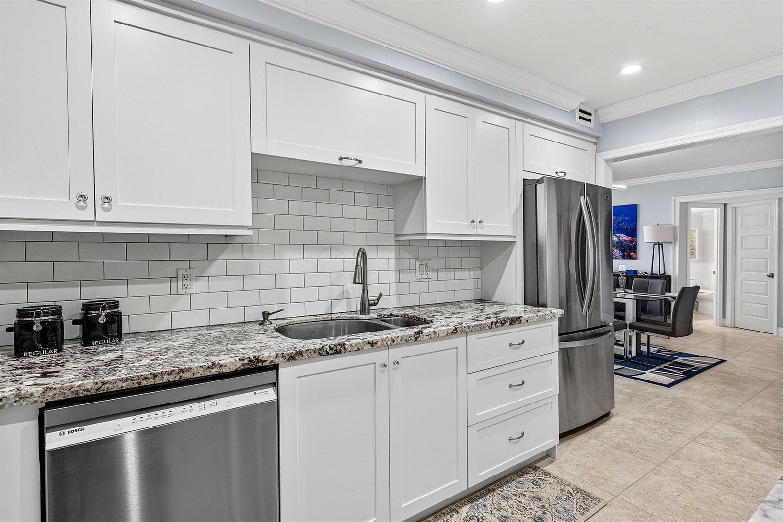 A kitchen features white cabinets, granite countertops, a stainless steel dishwasher, and subway tile backsplash — 2851 S Ocean Boulevard # m, Boca Raton FL 33432, BOCA RATON, FL
