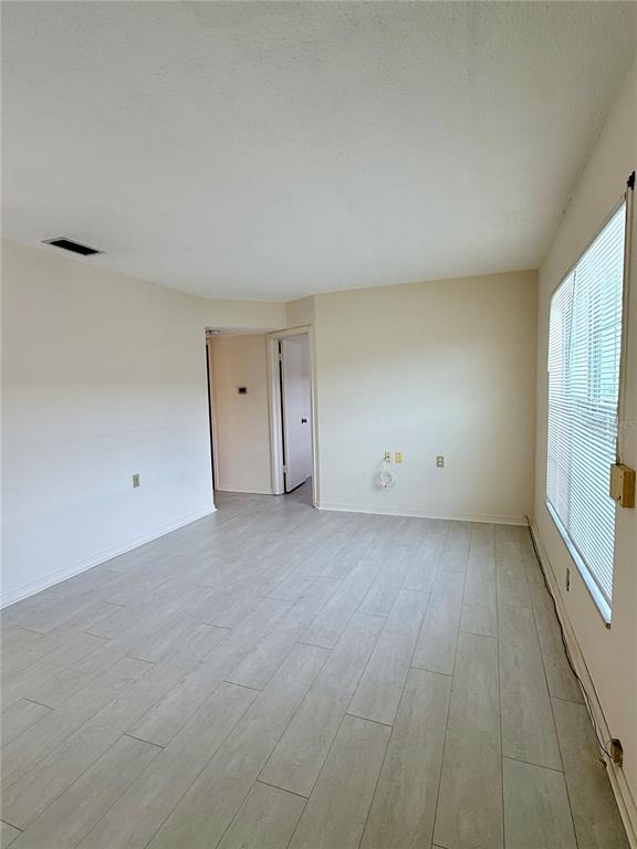 An empty room features light-colored wood-look tile flooring, beige walls, and a window with blinds — 7847 39TH TERRACE N, ST PETERSBURG, FL