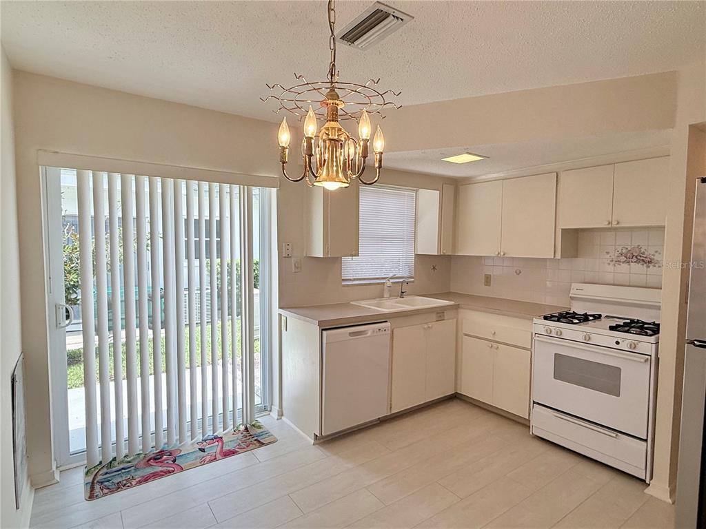 A kitchen with white cabinets, light tile flooring, and a sliding glass door to outside — 7847 39TH TERRACE N, ST PETERSBURG, FL