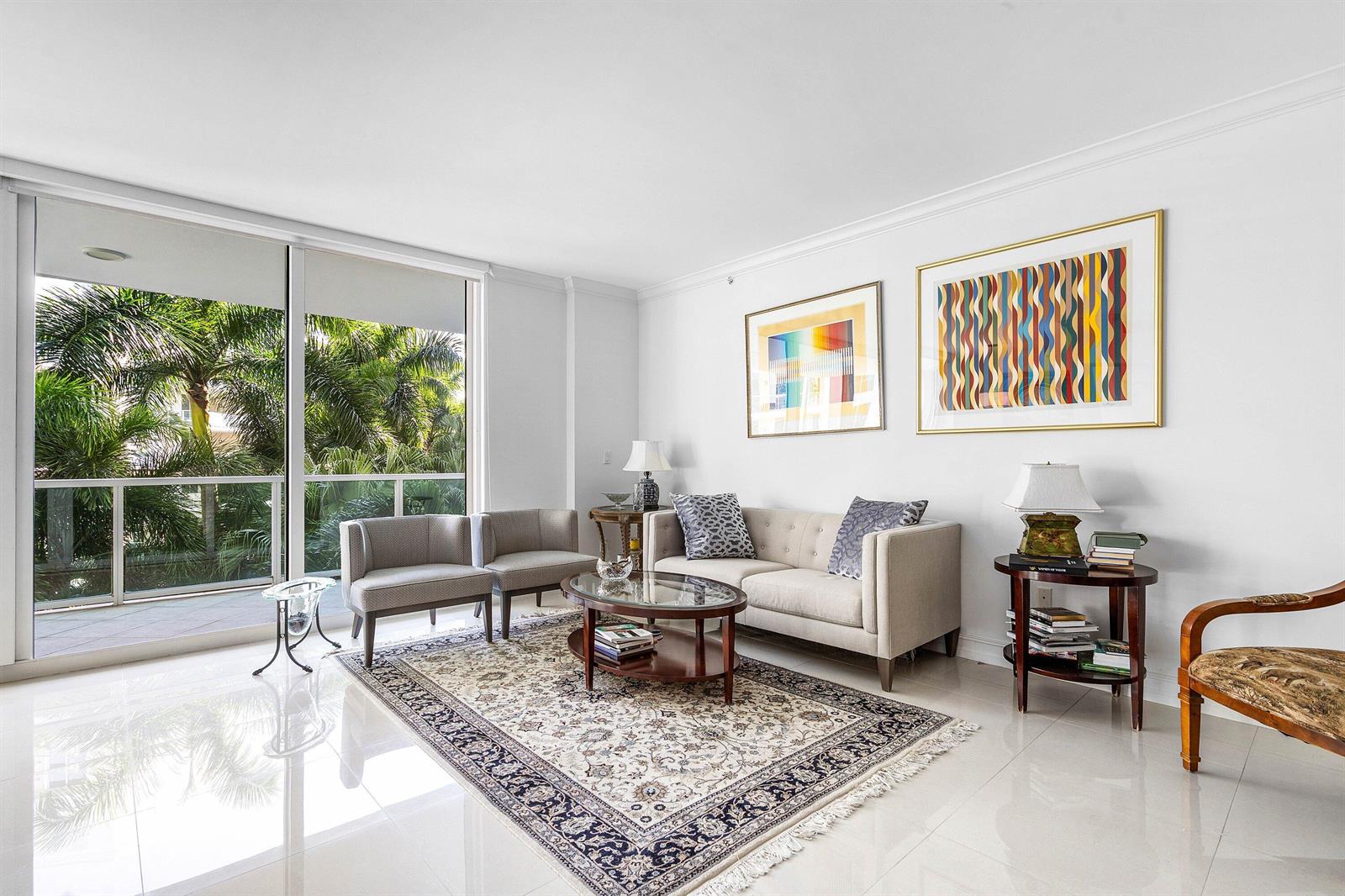 A bright living room features a beige sofa, patterned rug, and floor-to-ceiling windows with balcony — 500 SE Mizner Boulevard # A310, Boca Raton FL 33432, BOCA RATON, FL