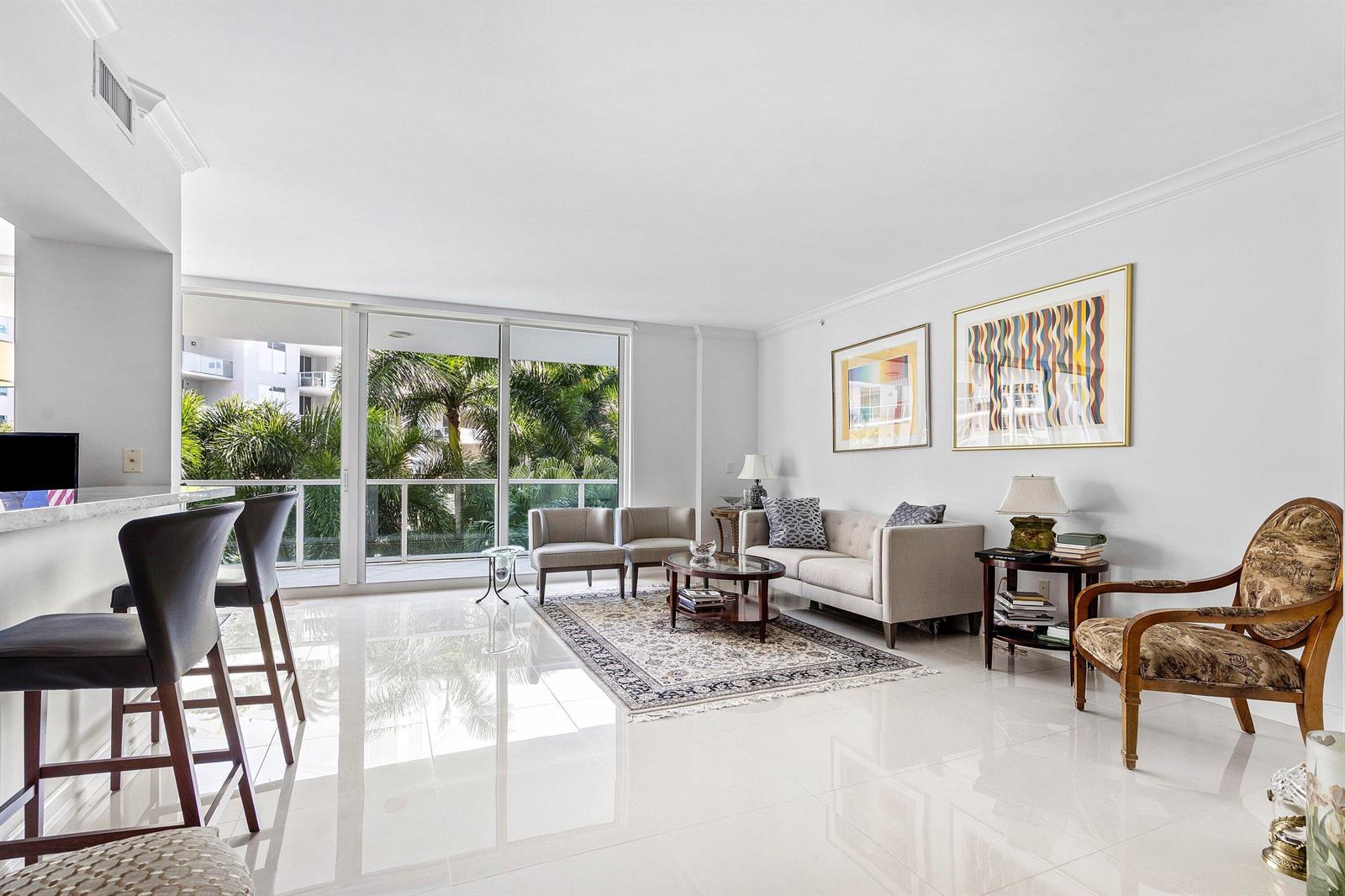A bright living room features white tile floors, a neutral sofa, and floor-to-ceiling balcony windows — 500 SE Mizner Boulevard # A310, Boca Raton FL 33432, BOCA RATON, FL