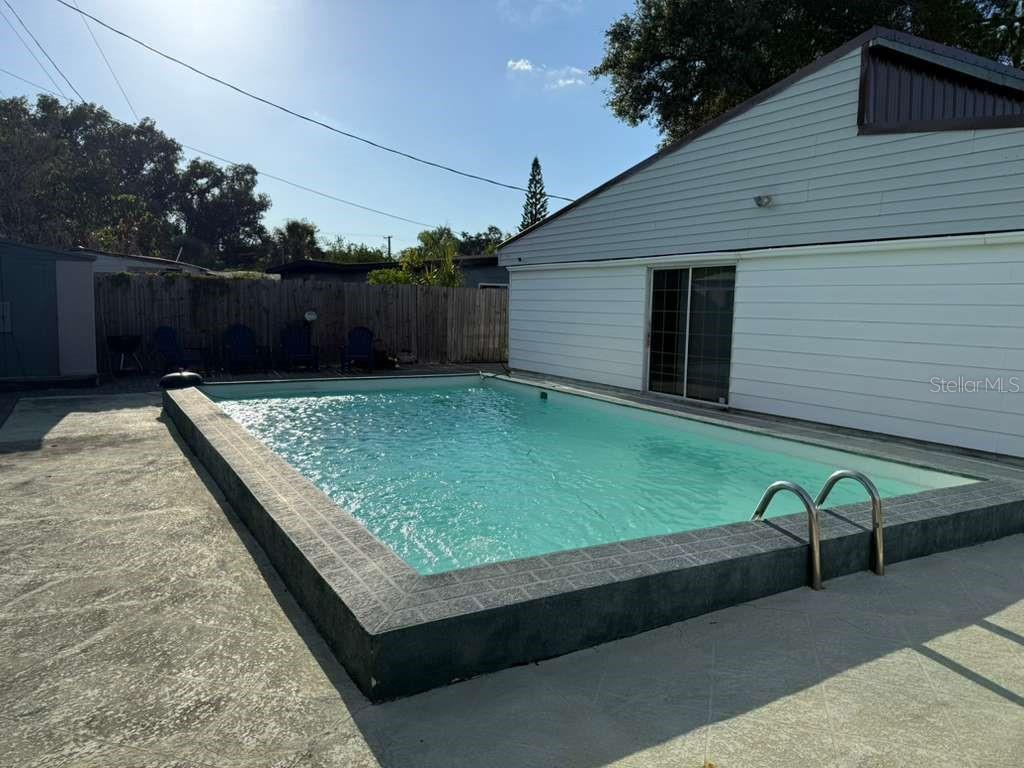 An elevated rectangular swimming pool sits on a concrete patio beside a white house — 7917 RIDEOUT ROAD, TAMPA, FL