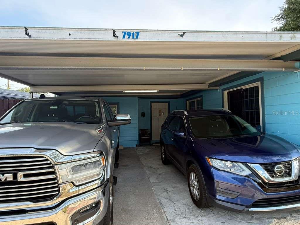 A carport with two parked vehicles sits in front of a light blue house — 7917 RIDEOUT ROAD, TAMPA, FL