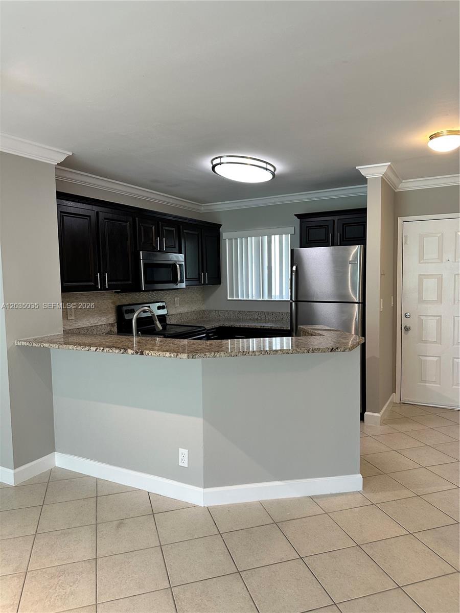 A kitchen features dark wood cabinets, granite countertops, stainless steel appliances, and tile flooring — MIRAMAR, FL