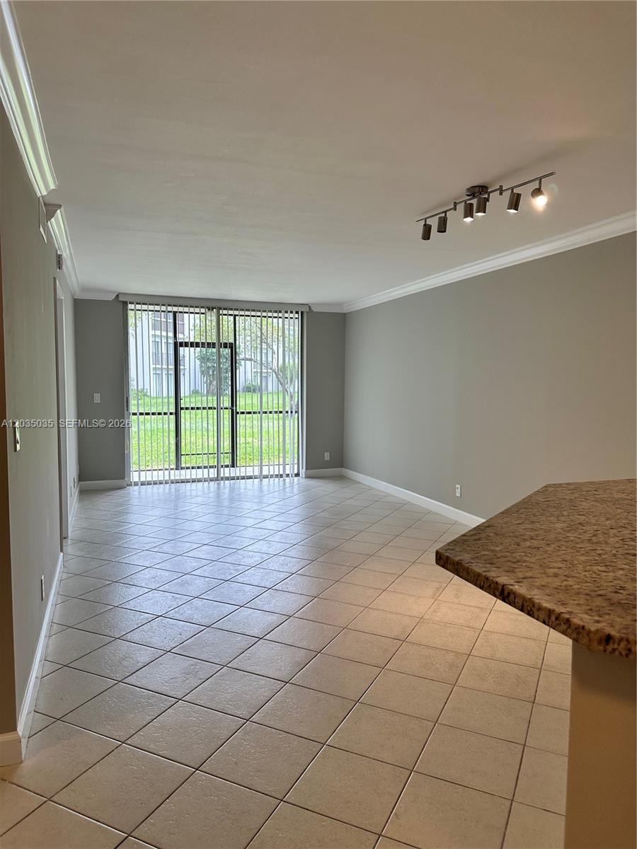 An empty living room features light-colored tile flooring, gray walls, and a sliding glass door — MIRAMAR, FL