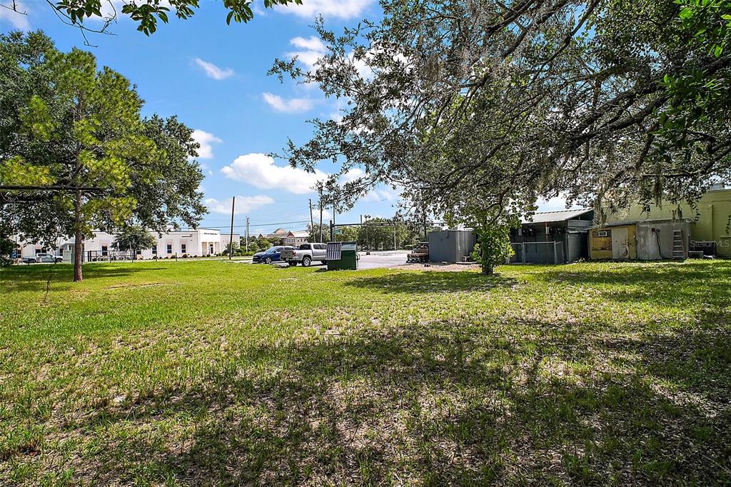 A grassy lot with trees, a dumpster, and nearby commercial buildings under a blue sky — 452 & 438 N PARK AVENUE, APOPKA, FL