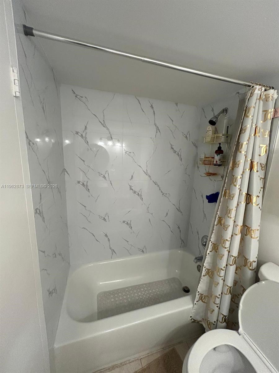 A bathroom features a white bathtub with marble-patterned wall tiles and a patterned shower curtain — 4314 NW 9th Ave # 3H, Deerfield Beach FL 33064, DEERFIELD BEACH, FL