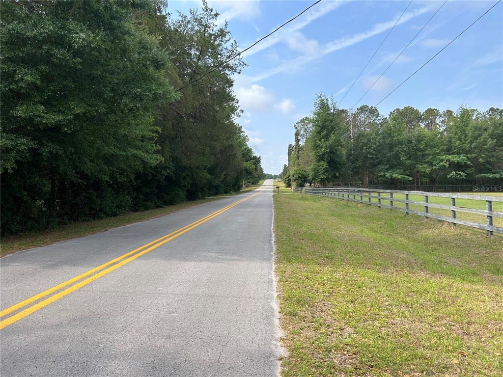 A paved road stretches into the distance between a wooded area and a wooden fence — 4580 NE 138TH TERRACE, WILLISTON, FL