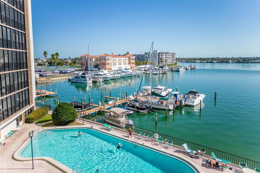 An elevated view of a swimming pool overlooking a marina with docked boats and buildings — 10355 PARADISE BOULEVARD UNIT 213, TREASURE ISLAND, FL