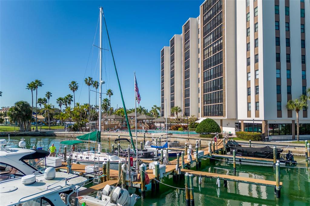 A tall apartment building stands beside a marina filled with boats docked at wooden piers — 10355 PARADISE BOULEVARD UNIT 213, TREASURE ISLAND, FL