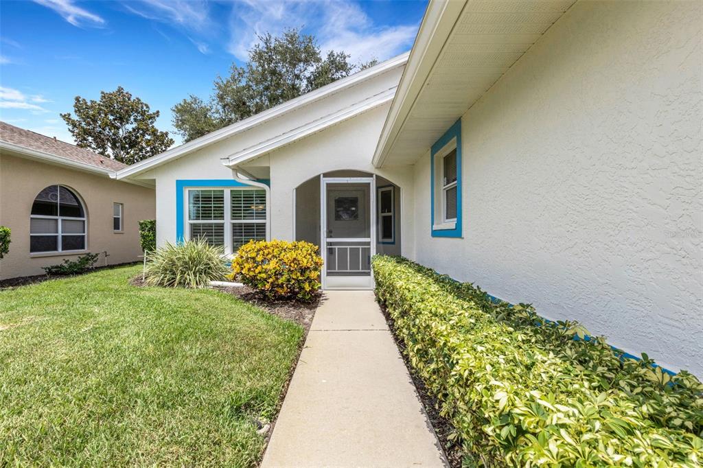 A concrete walkway leads to the front entrance of a house with white stucco walls — 4430 FERN DRIVE, BRADENTON, FL