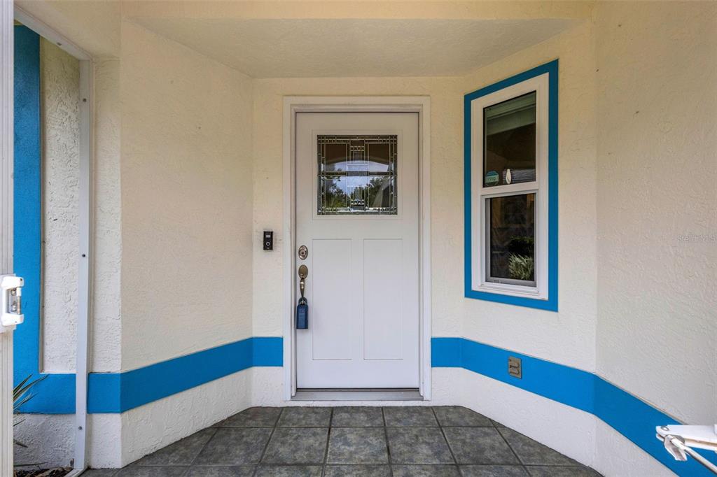 A white front door with a decorative glass window sits on a tiled porch entrance — 4430 FERN DRIVE, BRADENTON, FL