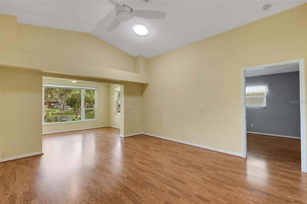 A living room with light yellow walls, wood-look flooring, a vaulted ceiling, and a ceiling fan — 4430 FERN DRIVE, BRADENTON, FL