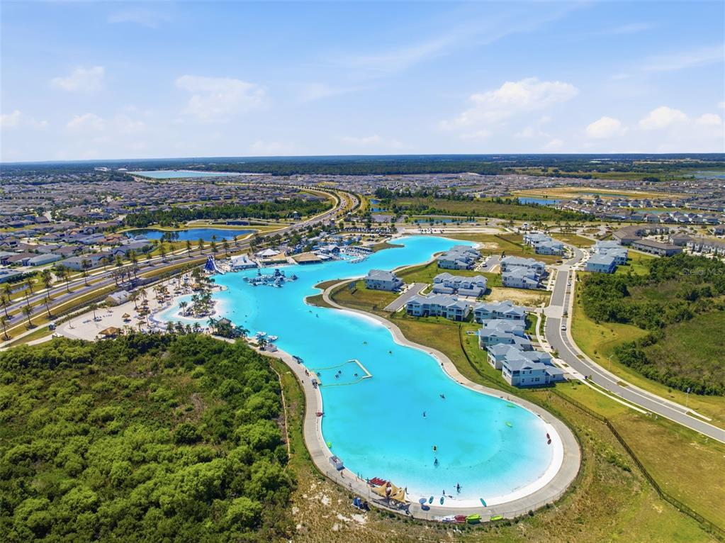 An aerial view of a large turquoise swimming lagoon surrounded by residential buildings and landscaping — 31555 BLUE PASSING LOOP, WESLEY CHAPEL, FL