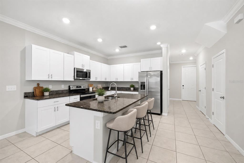 A modern kitchen features white cabinets, dark granite countertops, a center island, and stainless appliances — 31555 BLUE PASSING LOOP, WESLEY CHAPEL, FL