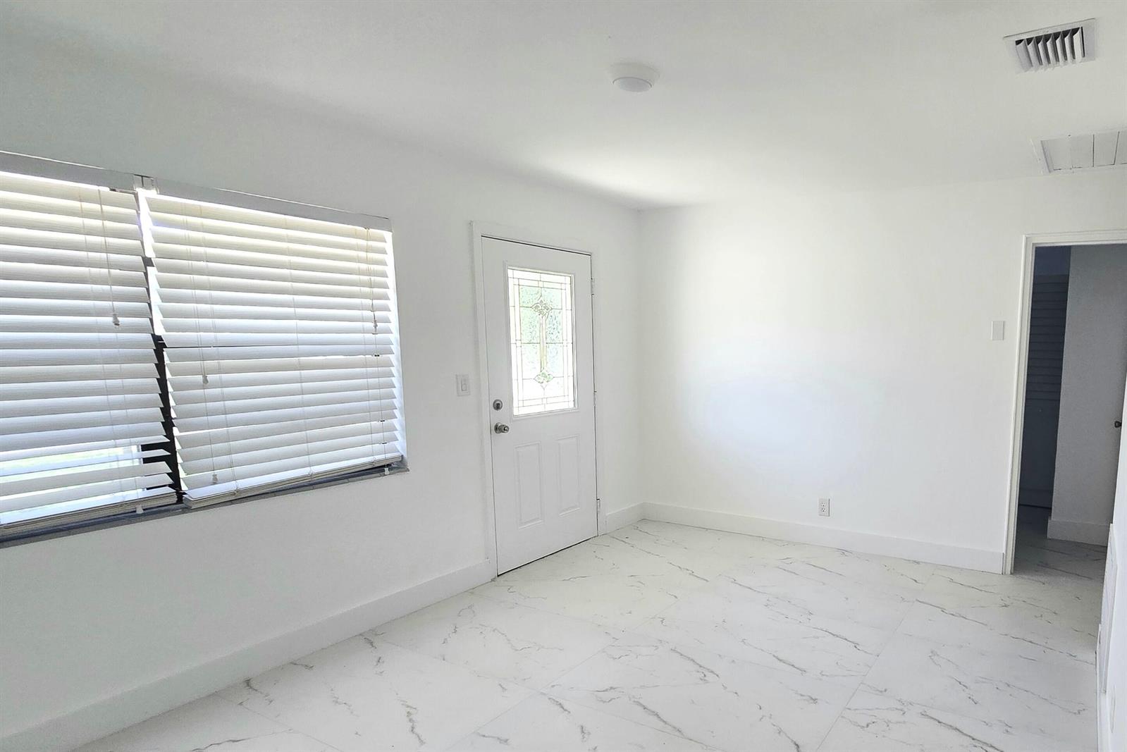 A bright room with white walls, white marble-look tile flooring, a window, and a door — 2849 NE 13th Avenue, Pompano Beach FL 33064, POMPANO BEACH, FL