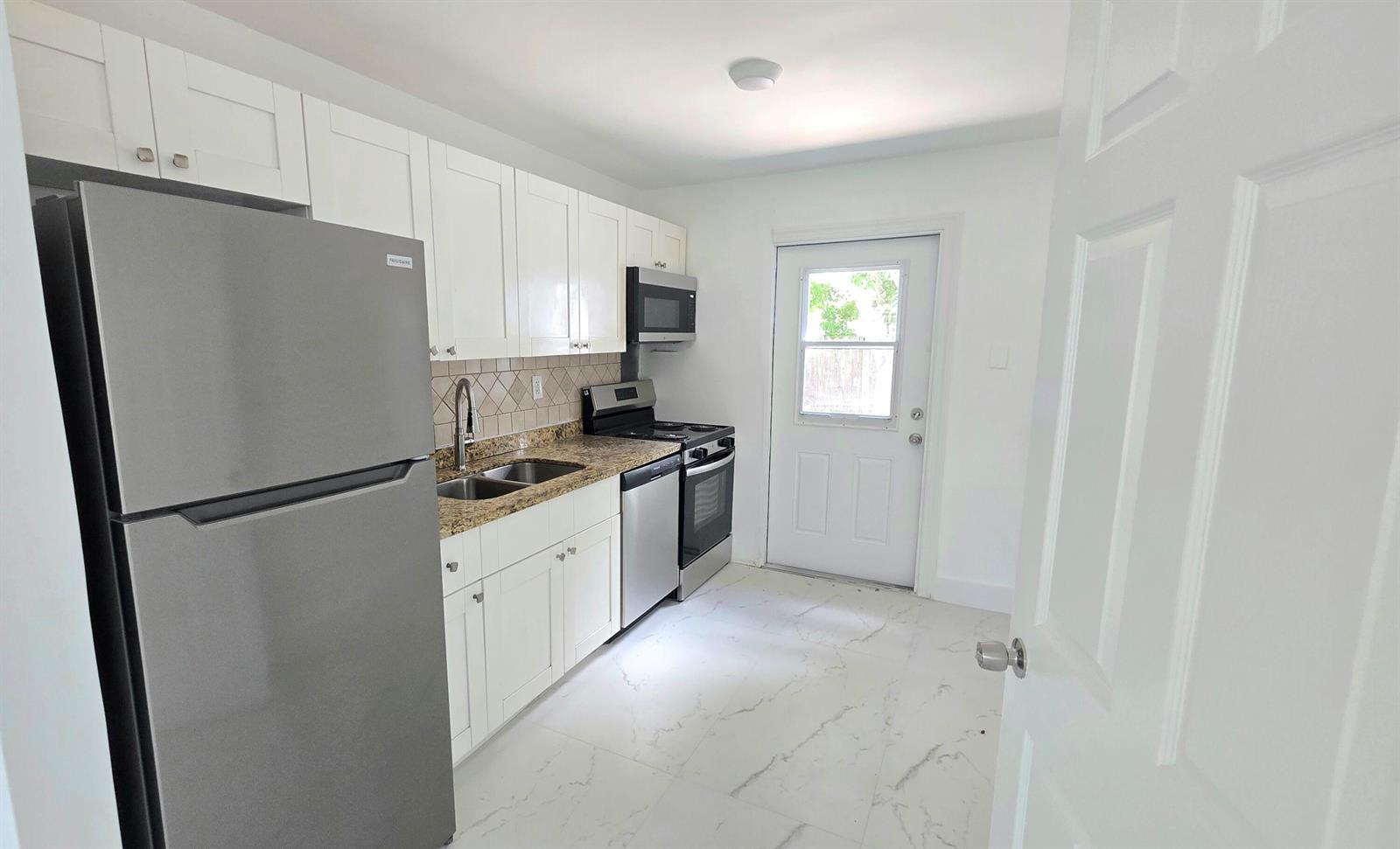 A kitchen features white cabinets, stainless steel appliances, granite countertops, and white marble-look tile flooring — 2849 NE 13th Avenue, Pompano Beach FL 33064, POMPANO BEACH, FL