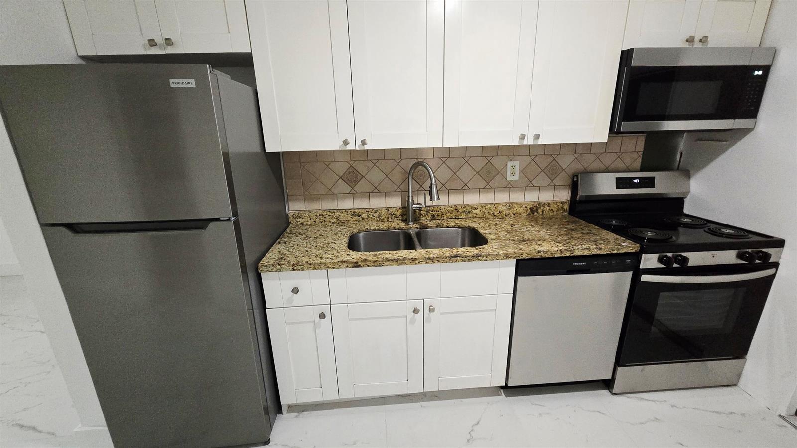 A kitchen features white cabinets, stainless steel appliances, and granite countertops with a tile backsplash — 2849 NE 13th Avenue, Pompano Beach FL 33064, POMPANO BEACH, FL