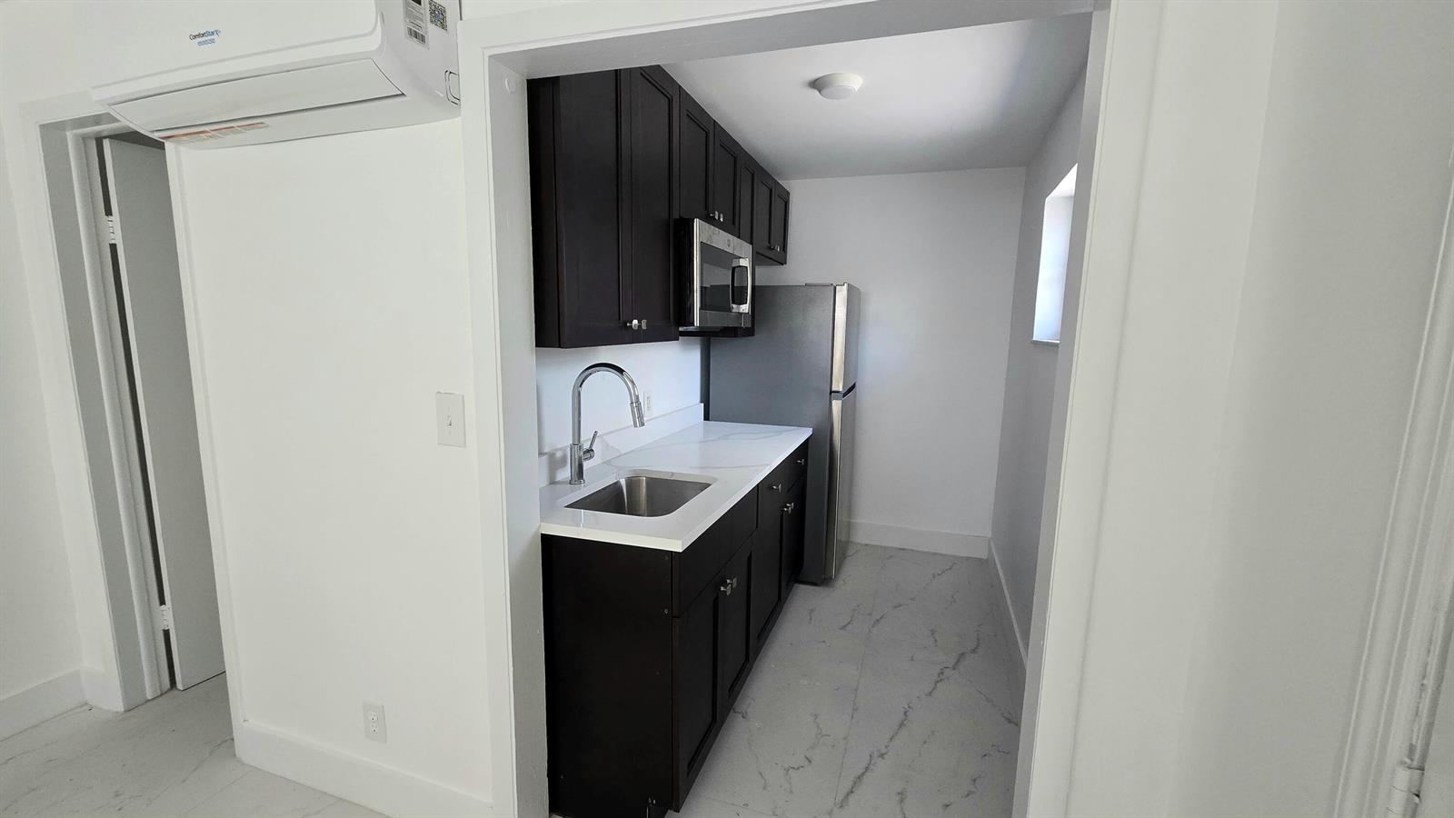 A galley kitchen features dark cabinets, white countertops, stainless steel appliances, and light-colored flooring — 2849 NE 13th Avenue, Pompano Beach FL 33064, POMPANO BEACH, FL