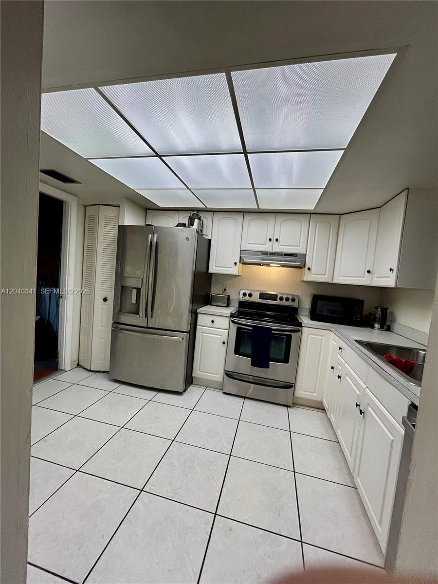 A kitchen features white cabinets, stainless steel appliances, and a large grid-style ceiling light — 7262 SW 1st St, Margate FL 33068, MARGATE, FL