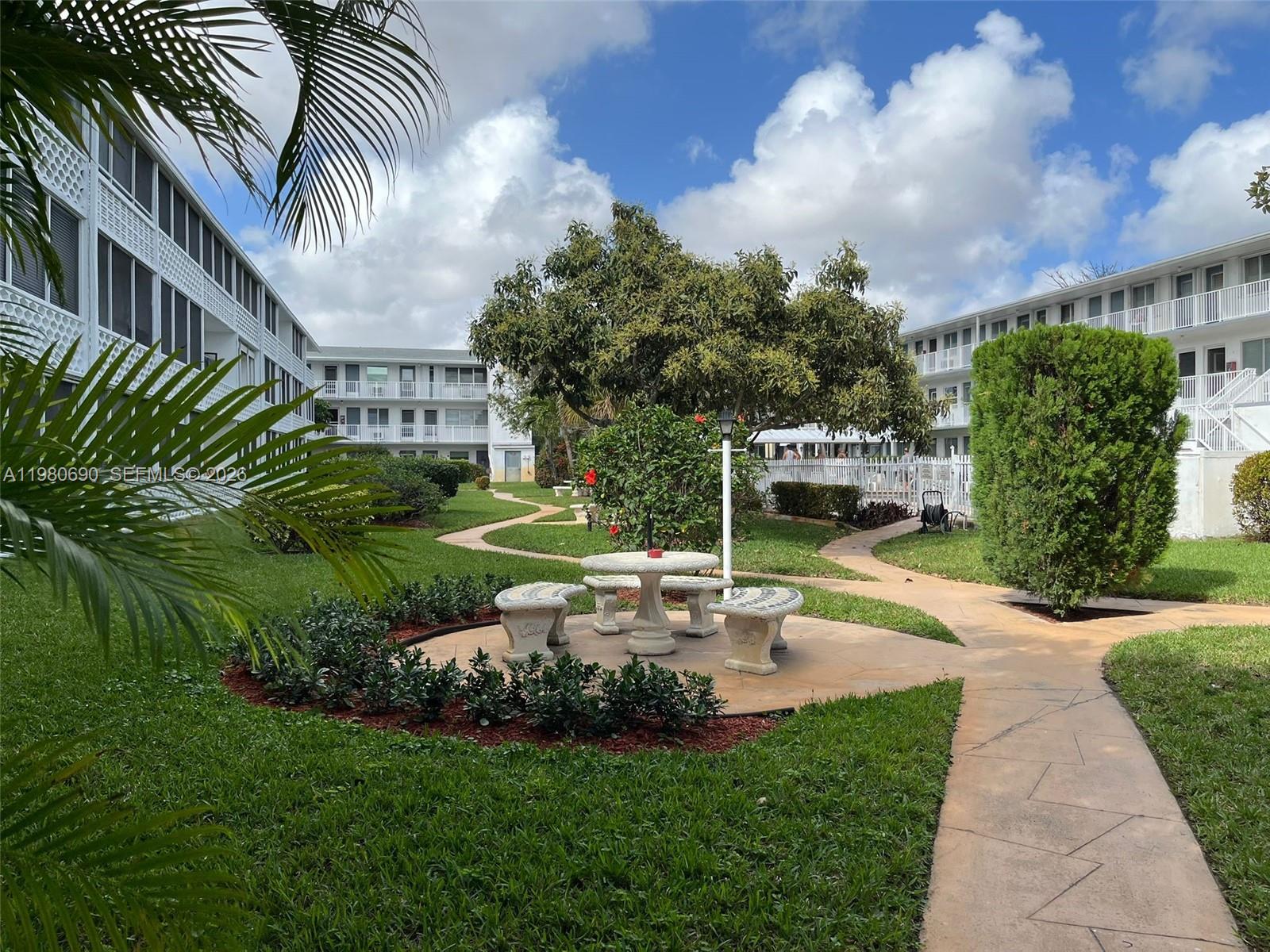 A courtyard with a stone table and benches surrounded by apartment buildings and landscaping — 15610 NE 6th Ave # 19C, Miami FL 33162, MIAMI, FL