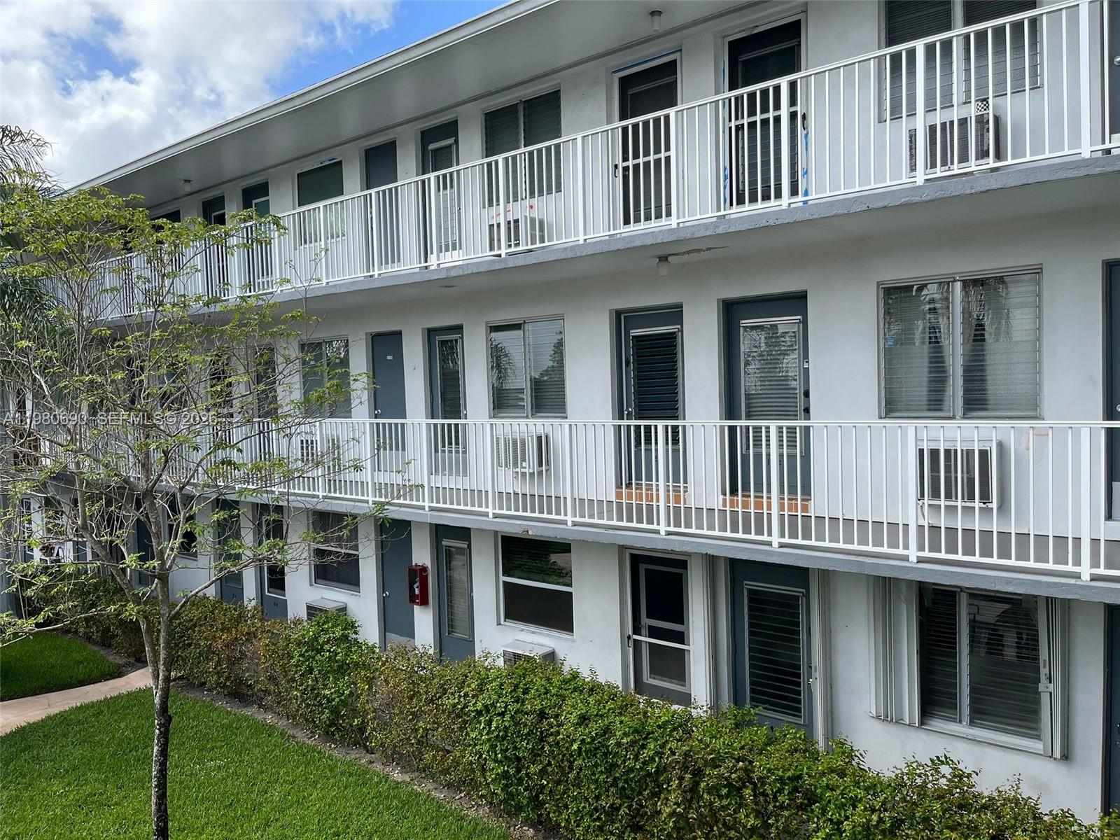 A three-story apartment building exterior features white railings, grey doors, and window air conditioning units — 15610 NE 6th Ave # 19C, Miami FL 33162, MIAMI, FL
