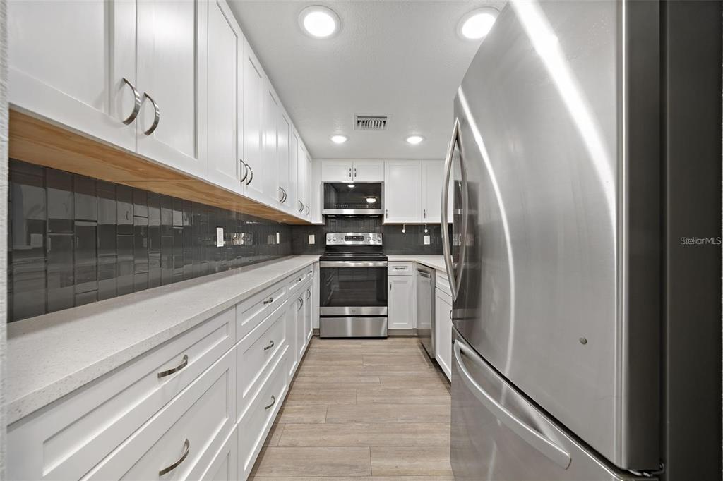 A galley kitchen features white cabinets, stainless steel appliances, dark tile backsplash, and light flooring — 4141 BAYSHORE BOULEVARD UNIT 1702, TAMPA, FL