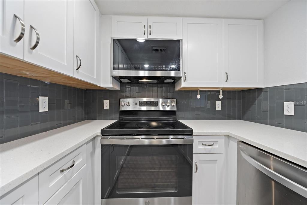 A kitchen features white cabinets, stainless steel appliances, a dark tile backsplash, and white countertops — 4141 BAYSHORE BOULEVARD UNIT 1702, TAMPA, FL
