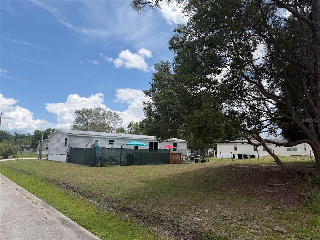 A view of a manufactured home with a fenced yard and a large tree — 15TH AVENUE, ORLANDO, FL