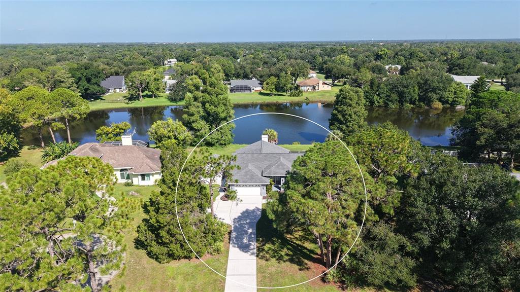 An aerial view shows a single-story house with a gray roof situated near a lake — 602 137TH STREET E, BRADENTON, FL