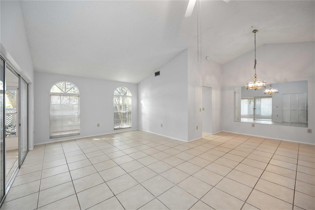 A bright, tiled living room features vaulted ceilings, arched windows, and a large wall mirror — 3411 57TH AVENUE DRIVE W UNIT 6, BRADENTON, FL