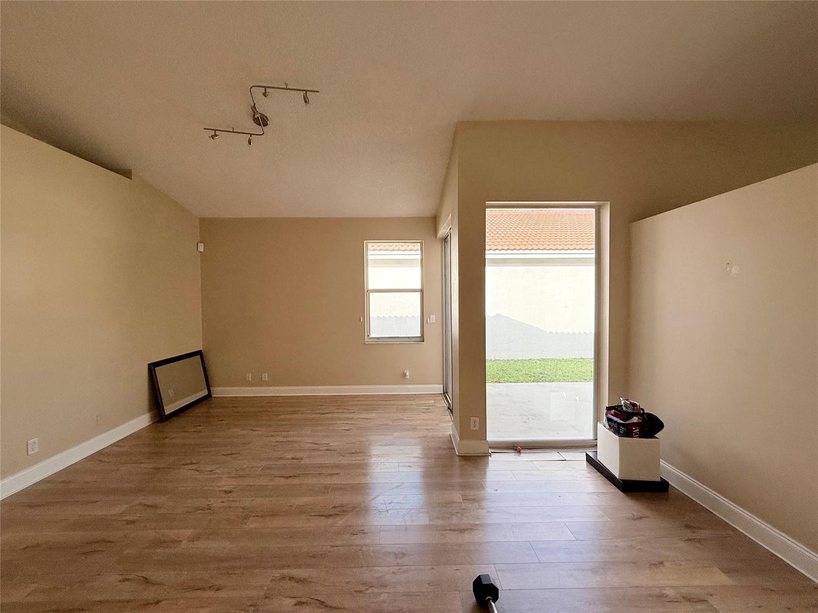 An empty room with light wood-look flooring, beige walls, a ceiling track light, and sliding doors — 4965 SW 153rd Avenue, Davie FL 33331, DAVIE, FL