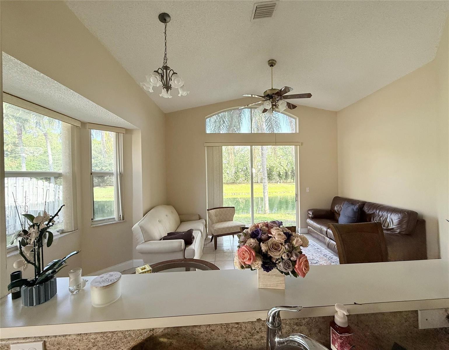 A living room with a vaulted ceiling, sliding glass doors, and views of a pond — 4965 SW 153rd Avenue, Davie FL 33331, DAVIE, FL